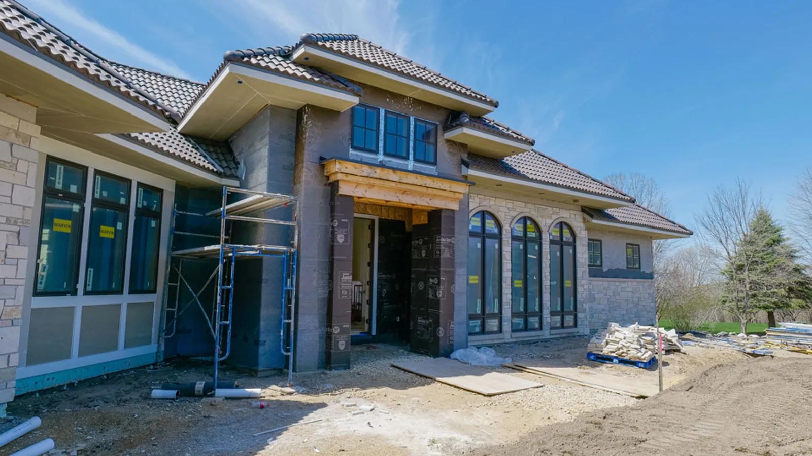 Stucco house under construction with scaffolding, tile roof and bare dirt yard