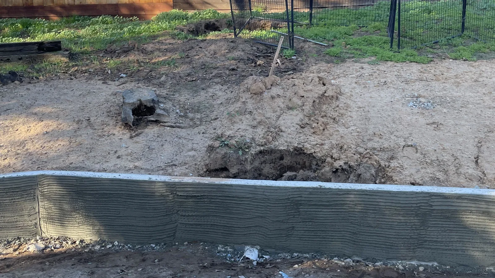 Poured retaining wall with a scratch coat running across a cleared yard