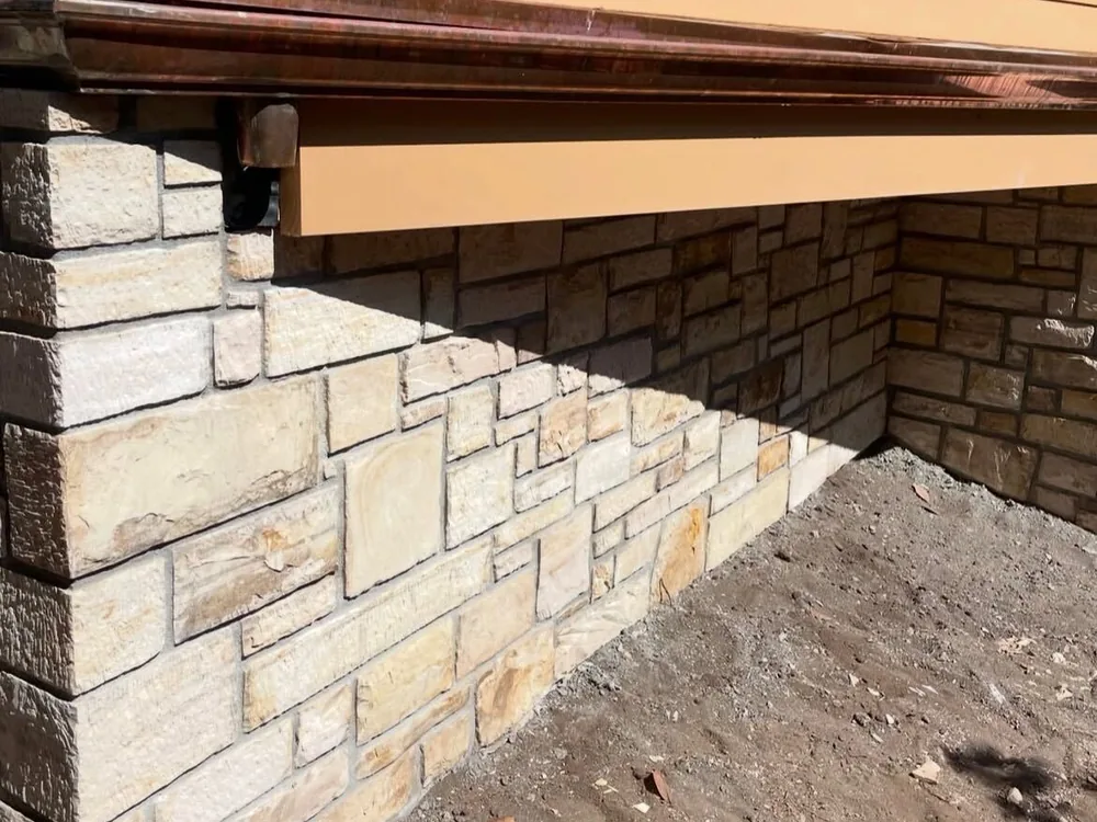 Two-tone stone veneer wrapping an outside corner under a copper cap