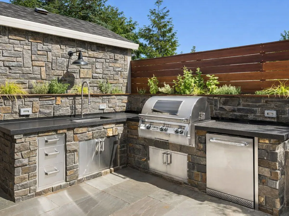 Stone-faced outdoor kitchen island with built-in gas grill and stainless drawers