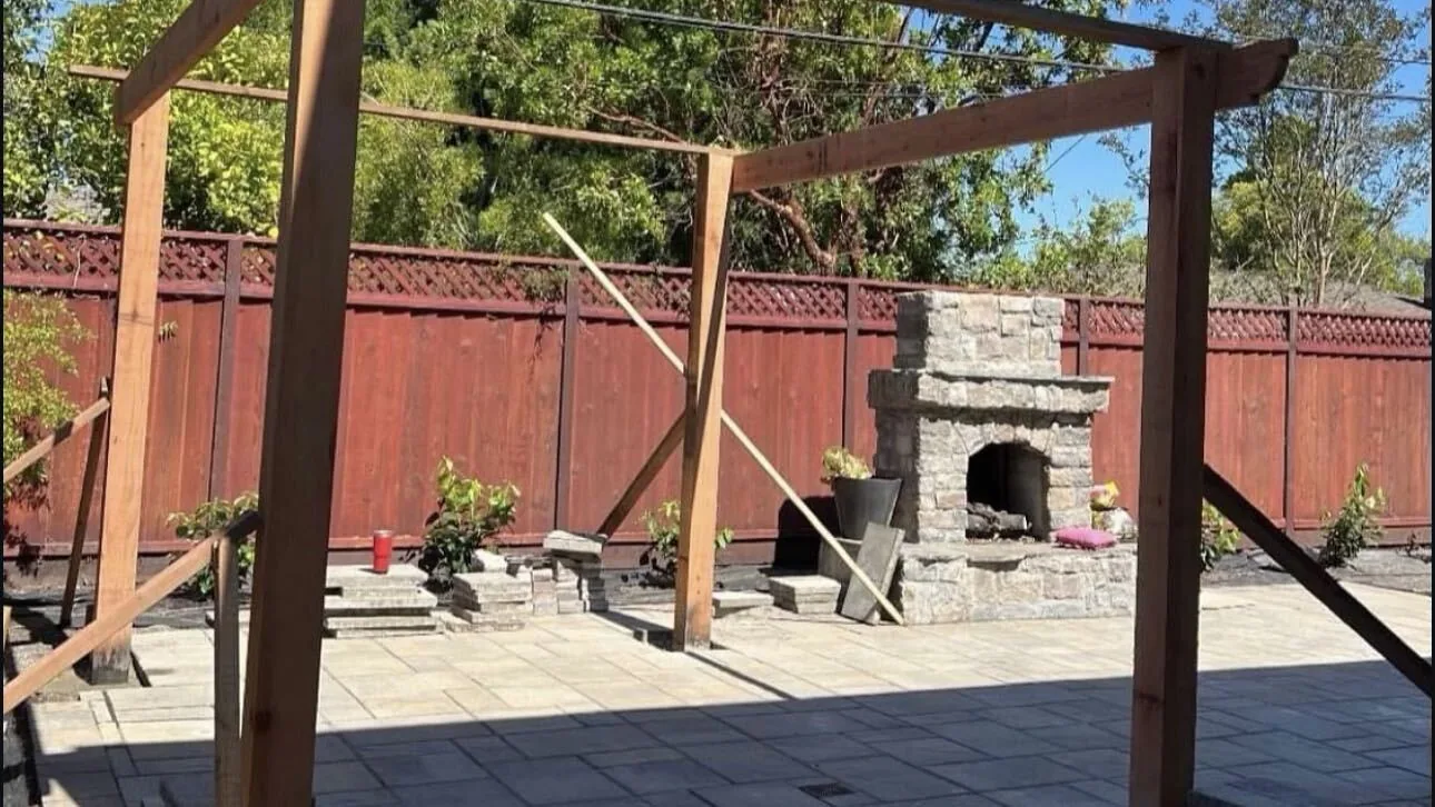 Redwood pergola frame over pavers with a stone fireplace by Aguilar and Sons Construction