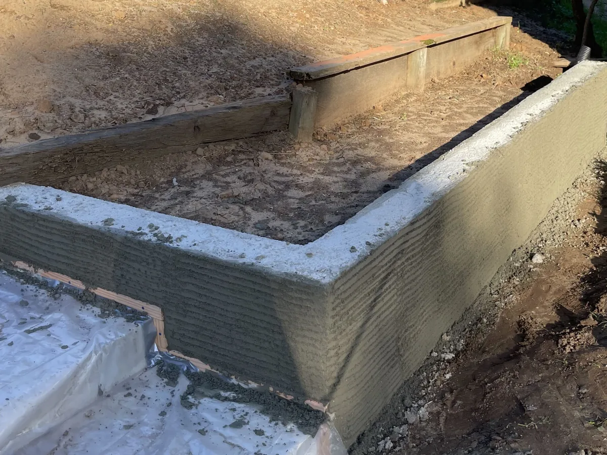 Poured retaining wall corner finished with a scratch coat on a planted slope