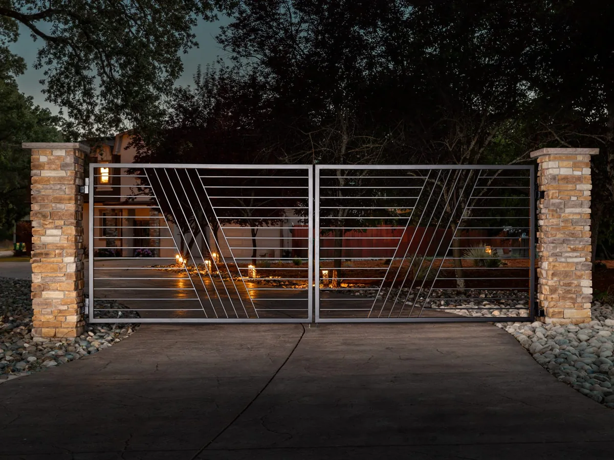 Iron driveway gate between stacked stone columns above a concrete drive